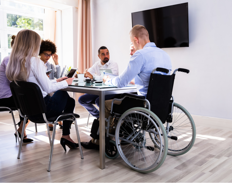 group of people sitting around a table, one person is in a wheelchair
