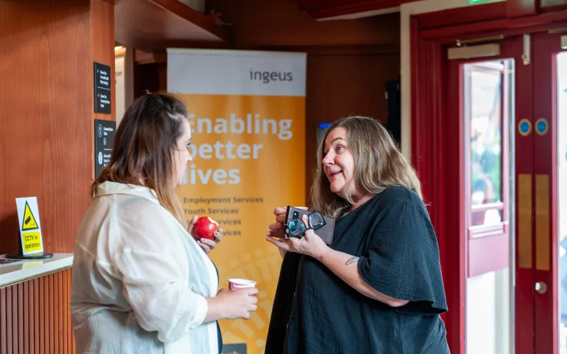 Two women stood by an Ingeus banner stand in discussion