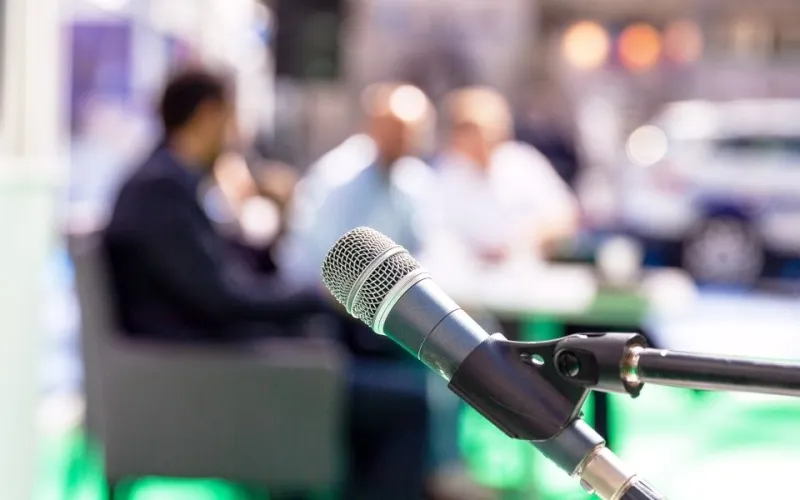 blurred photo of people at a roundtable discussion with microphone in foreground