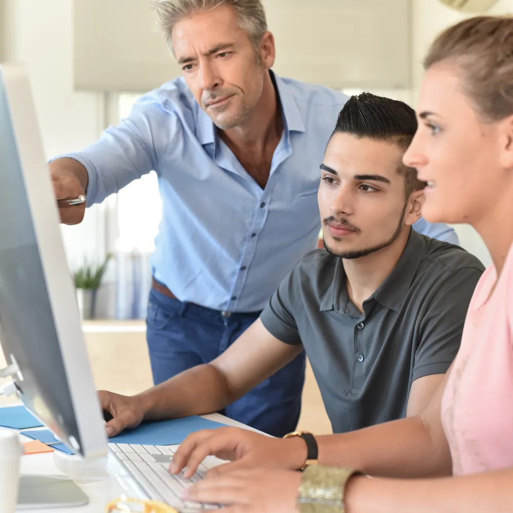 young adults around computer with teacher