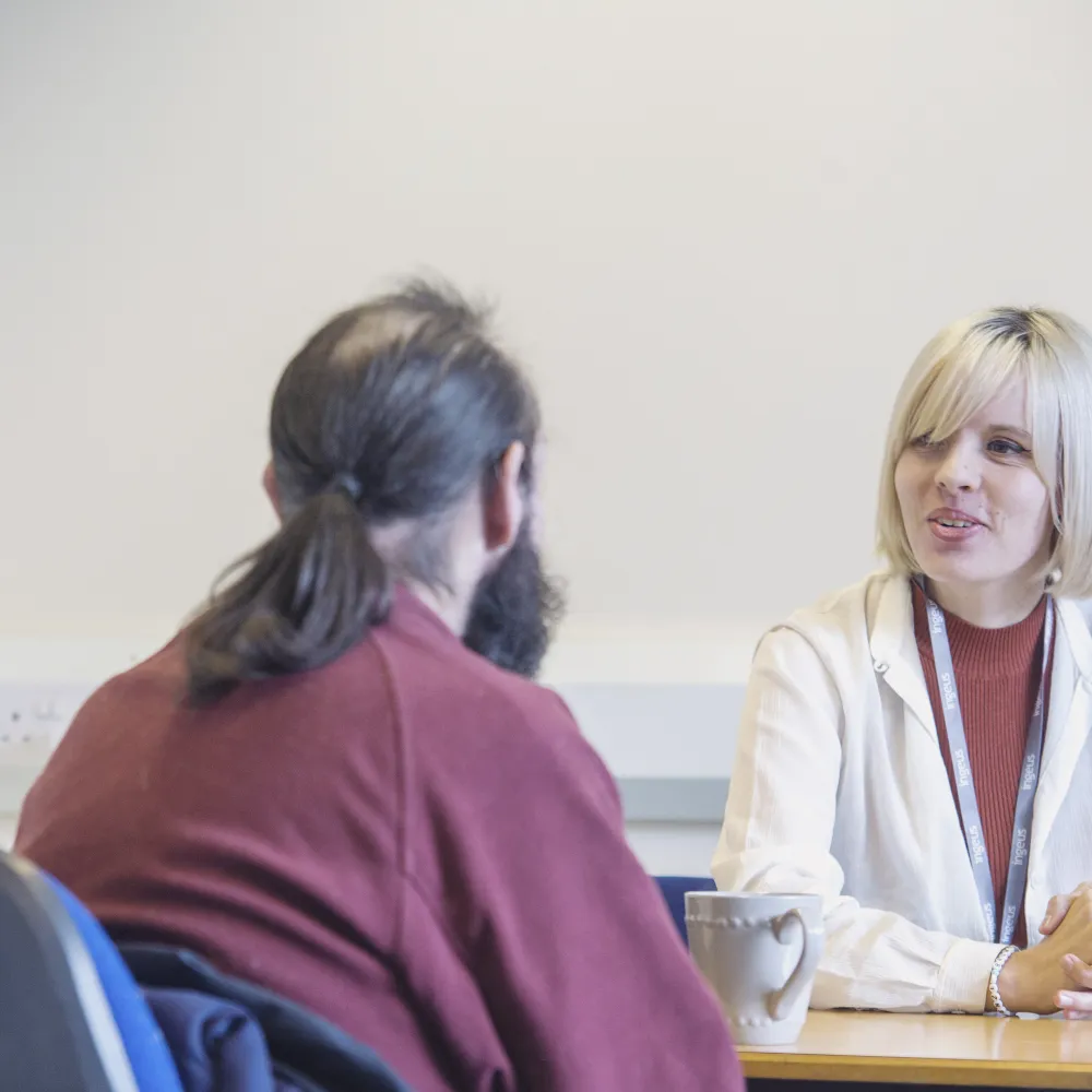 woman at desk with white coat and long haired man