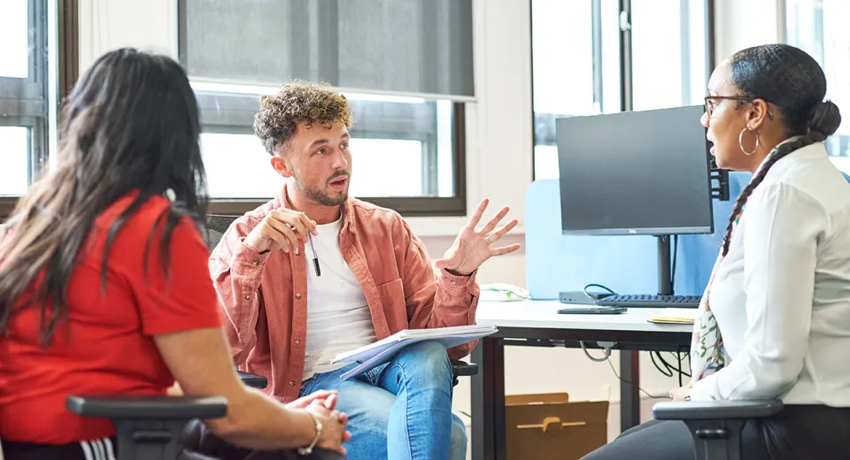 man and two women talking around desk